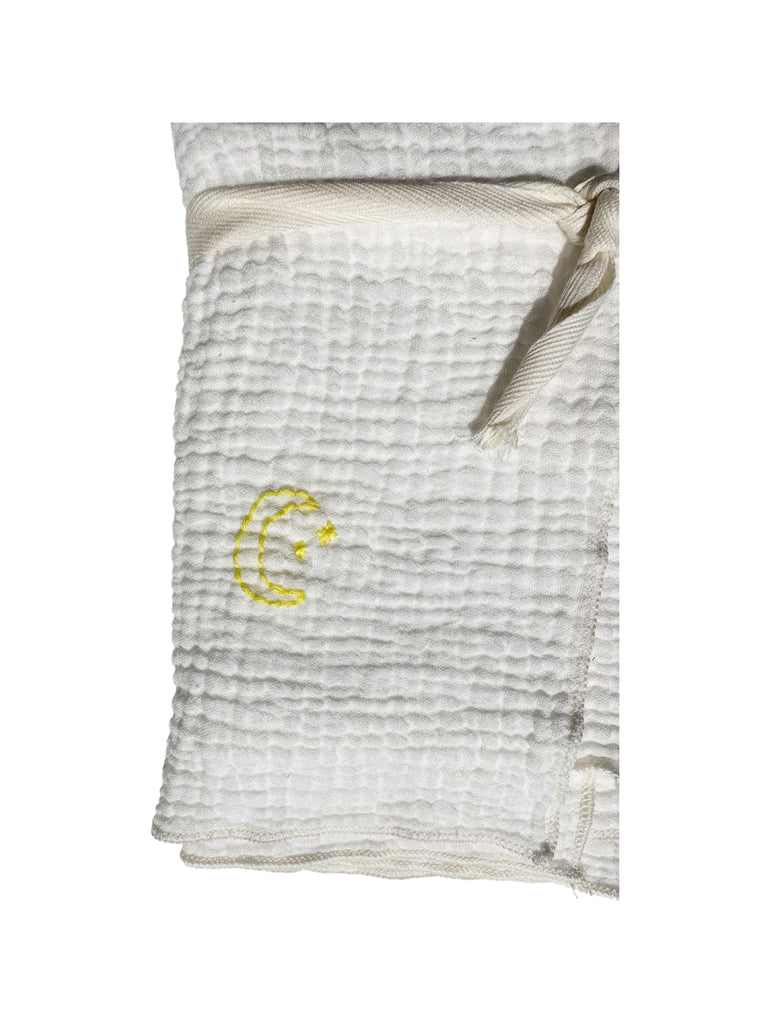 A close up of a white dish towel with a bubble/raised soft looking texture folded up with bright yellow embroidery of a crescent moon