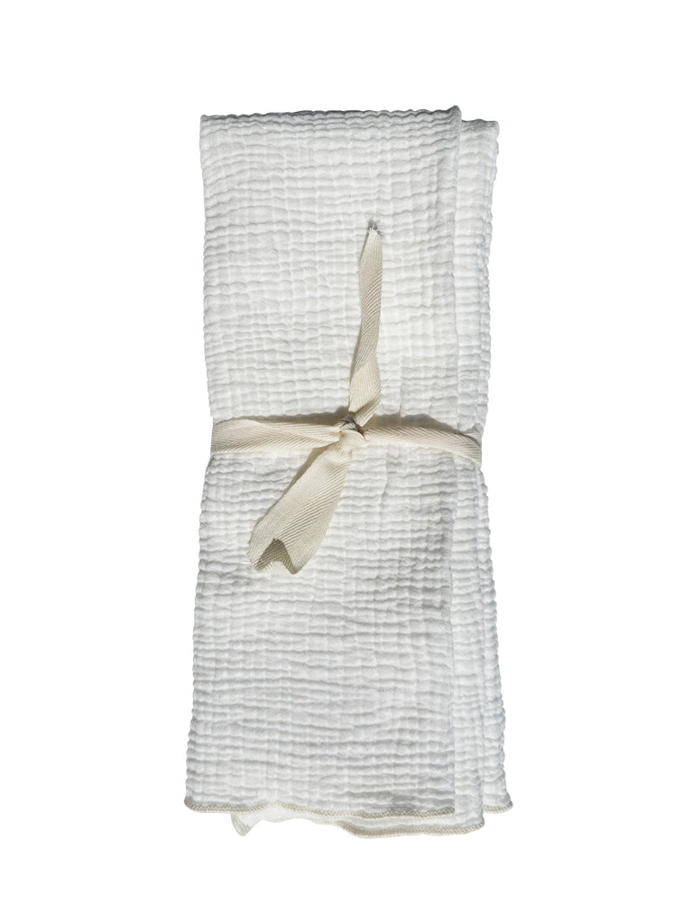 A folded up dish towel with a soft looking bubble/raised texture with a single ivory ribbon tied around it against a white background 